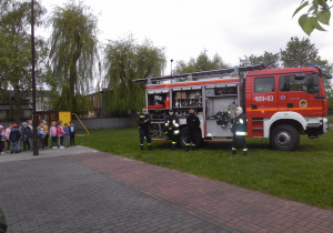 Strażacy na terenie przedszkola prezentują wyposażenie i przeznaczenie sprzętu w jaki jest wyposażony bojowy wóz strażacki